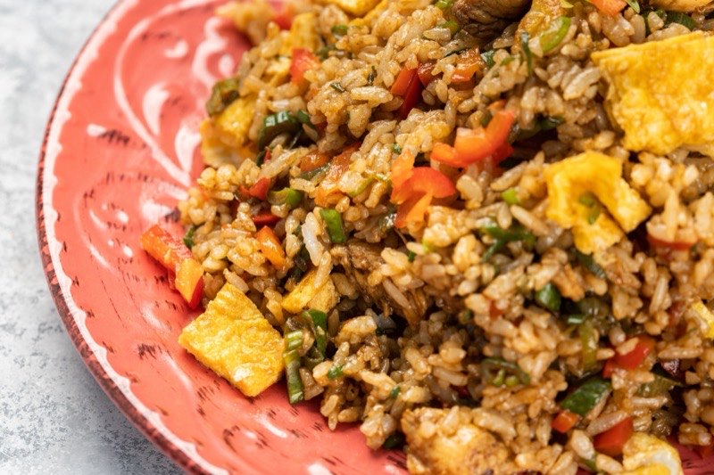 Fried rice with red pepper, spring onion and egg, served close-up on a coral plate.