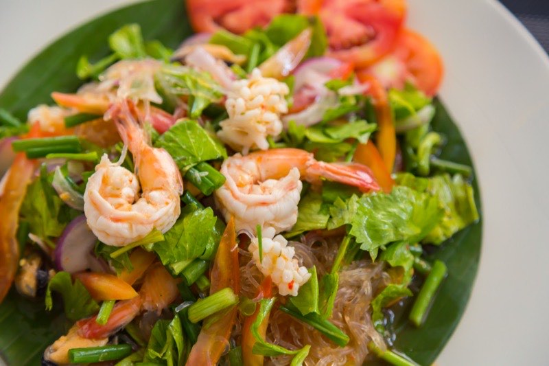 Thai shrimp salad with glass noodles, fresh herbs, red onion and tomato on a banana leaf.